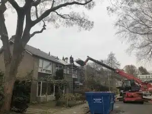 Dakdekkers op het dak van een rijtjeswoning in Wageningen, met verreiker en afvalcontainer