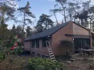 Dakdekkers leggen nieuwe donkere dakpannen op een woning in het bos in Wolfheze